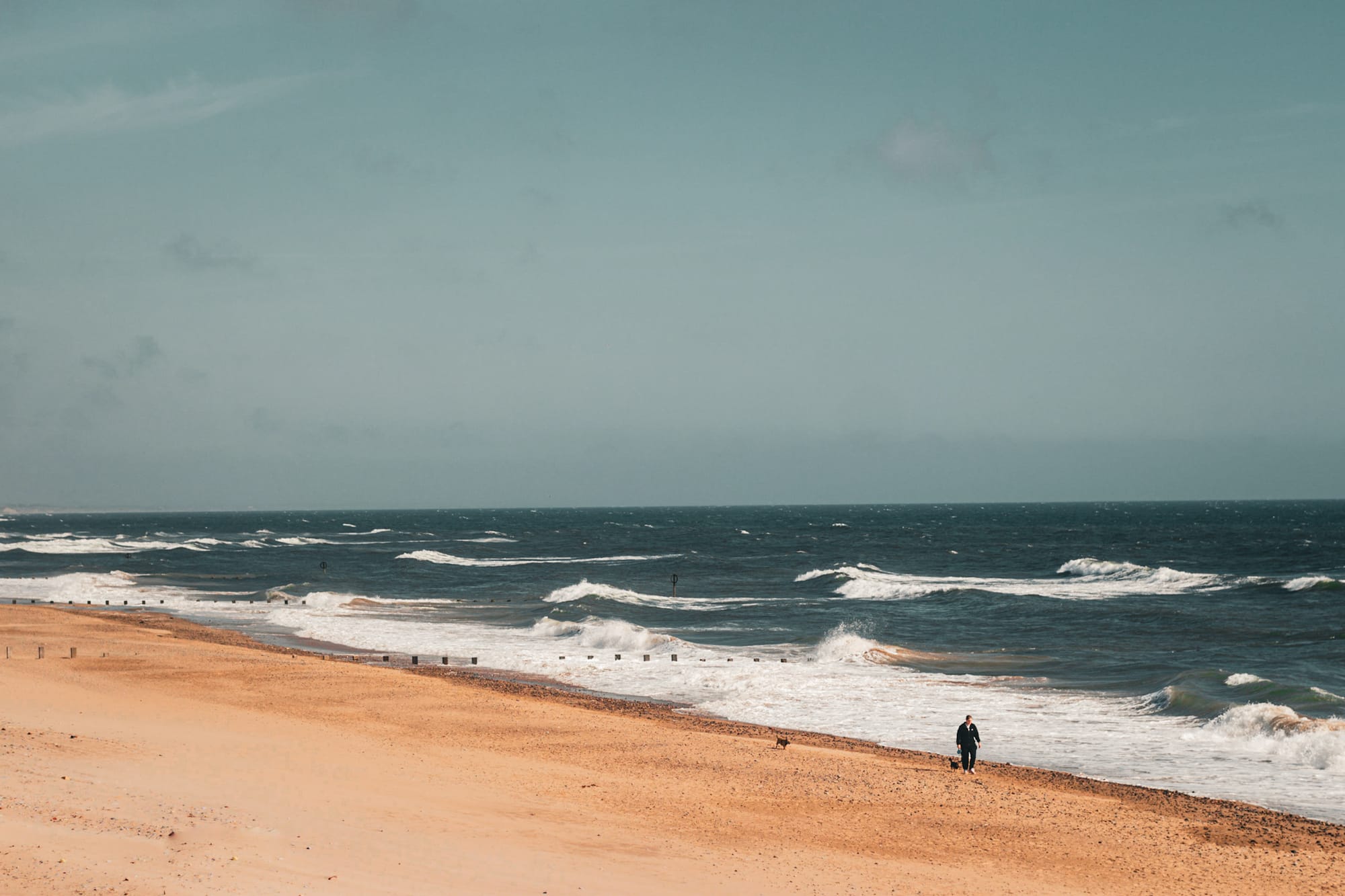 Waves crashing on Aberdeen Beach with a solitary walker on the sandy shore under a clear sky.