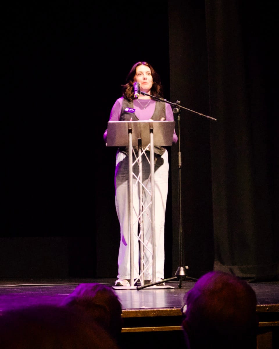 A woman stand behind a podium on a darkened stage
