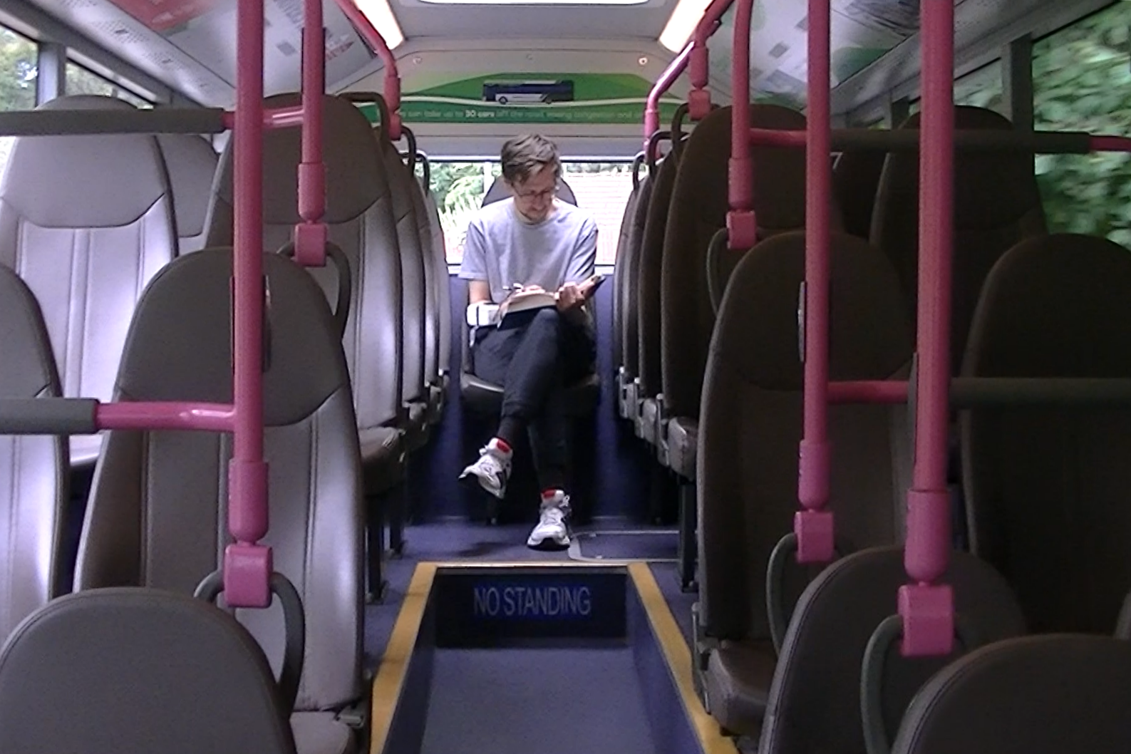 Artist Andrey Chugunov sits alone on the top deck of a moving bus, writing in a notebook.