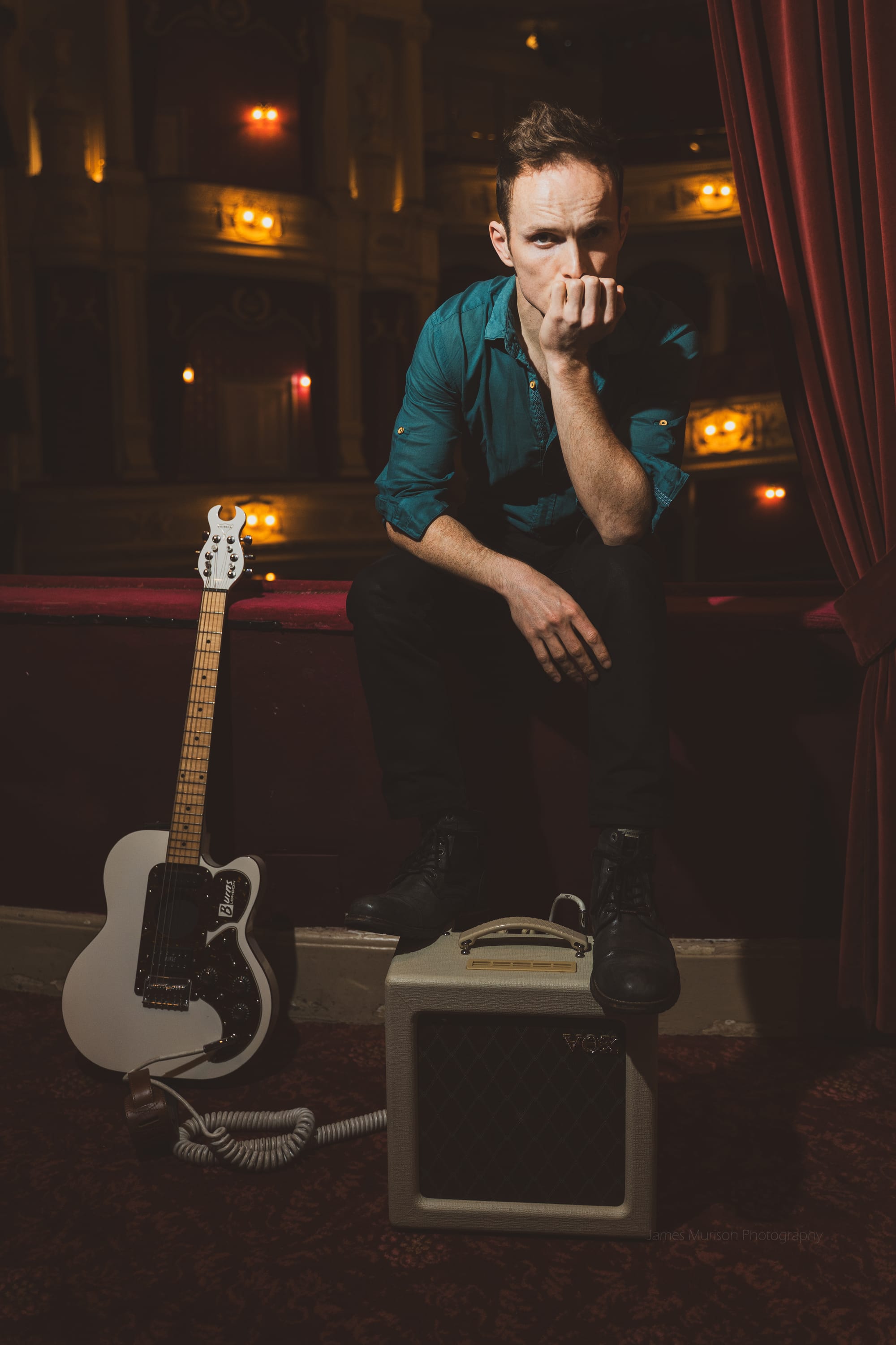 Oliver Richard sitting with white guitar and amplifier