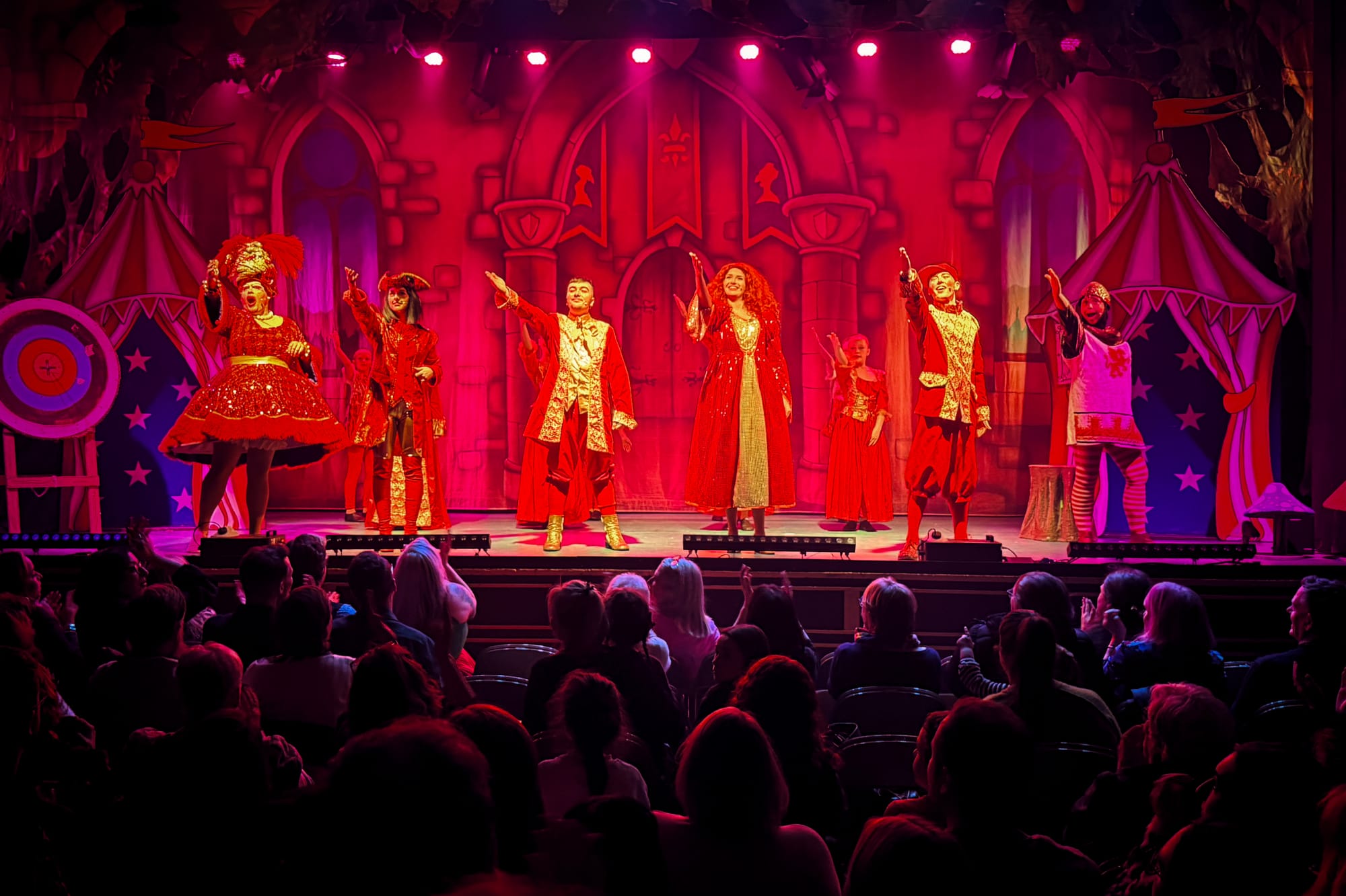 Cast of Robin Hood panto on stage in red and gold costumes with castle backdrop