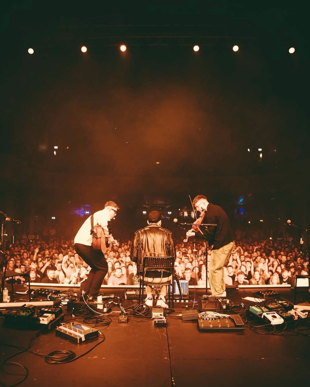 Talisk performing on stage to packed crowd, fiddle, concertina and guitar visible