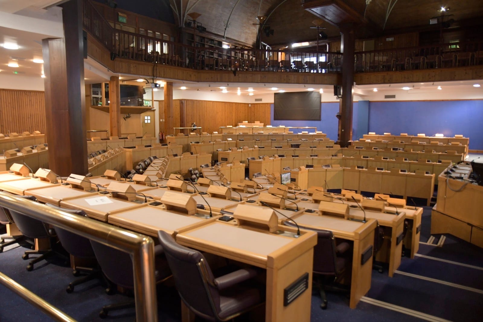 Empty debating chamber with tiered wooden desks and microphones at King's Conference Centre