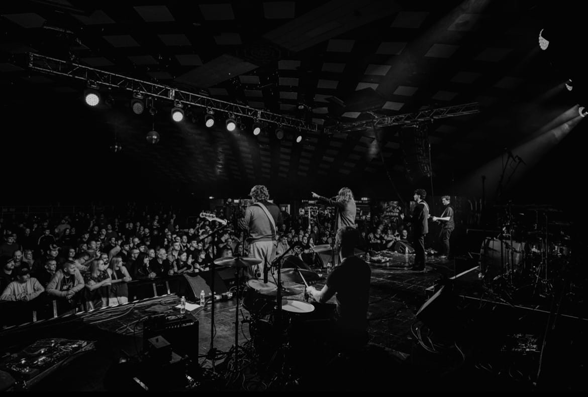The Capollos perform live in a packed venue, captured in black and white from behind the drummer.