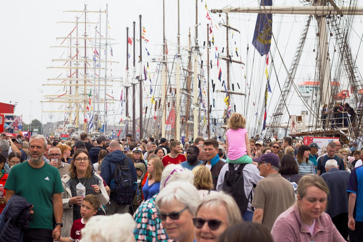 A dense crowd lines Regent Quay in Aberdeen with tall ships and masts rising in the background.