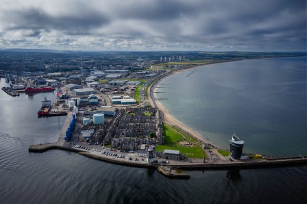 Aerial view of Aberdeen showing the harbour entrance and the Fittie area. The scene includes industrial docks and beachfront.