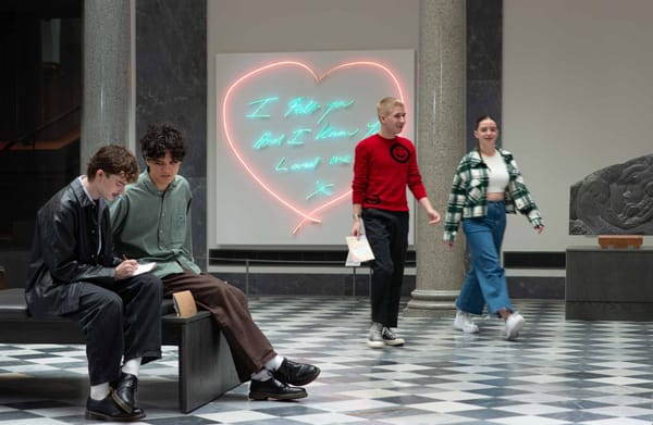 Aberdeen Art Gallery, two men sit by a neon heart art, while two others walk past on a checkered floor