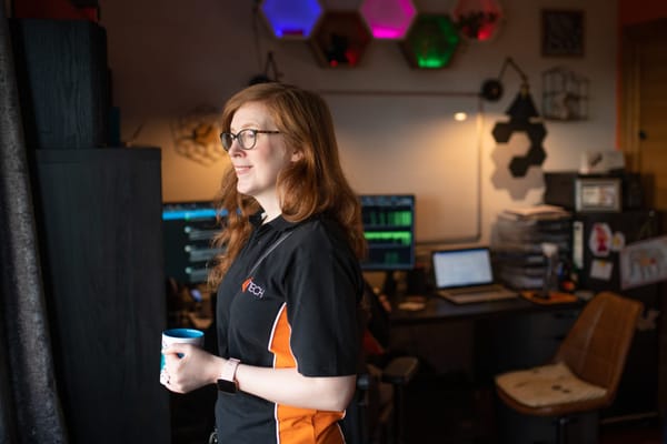 Caroline Laurenson smiling with a mug in hand, standing in a colourful tech-filled workspace.
