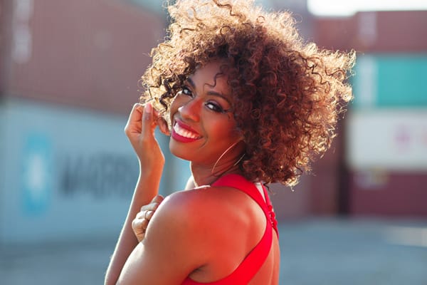 Sidonie Smith smiles at the camera in a red dress, standing outside with sunlight in her curly hair.