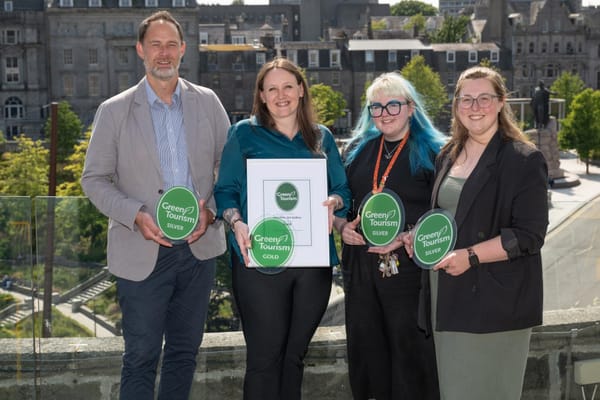 Four people holding Green Tourism plaques on a rooftop in Aberdeen, with buildings in the background.