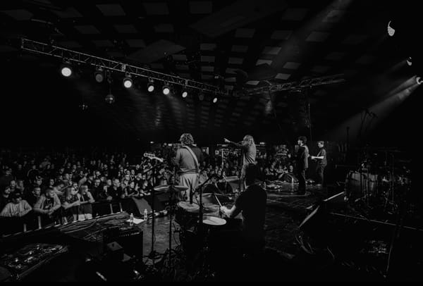 The Capollos perform live in a packed venue, captured in black and white from behind the drummer.