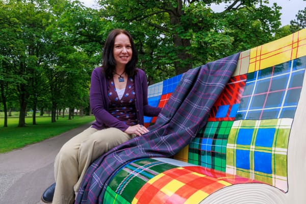 Sandra Russell sits on a painted bench shaped like an open book, covered in colourful tartan patterns.
