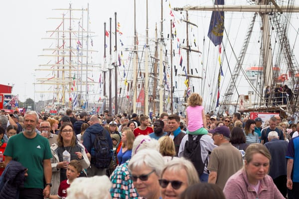 A dense crowd lines Regent Quay in Aberdeen with tall ships and masts rising in the background.