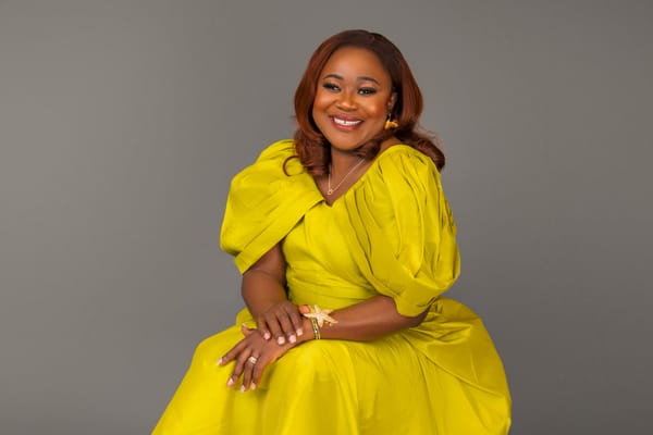 Oluwakemi Eseyin seated, smiling in a bold yellow dress against a plain grey background.
