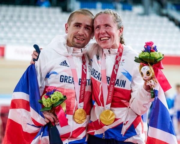 Neil Fachie and Lora Fachie embrace, gold medals round their necks and draped in a union jack flag.