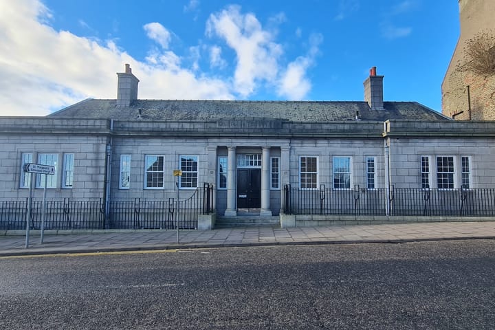 Historic granite building with symmetrical windows, chimneys, railings, under blue sky.