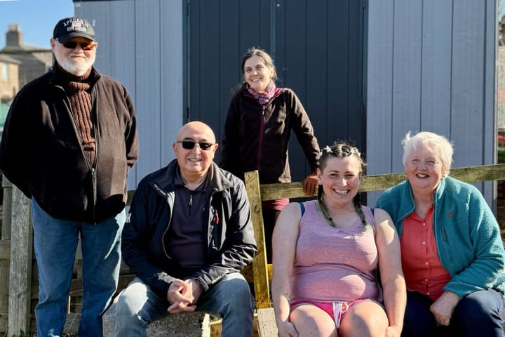 Five plotholders smiling in front of a new grey shed at Tullos Crescent Allotments in Aberdeen.