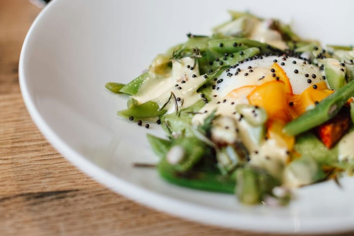Close-up of a plated dish with egg, greens and dressing on a wooden table