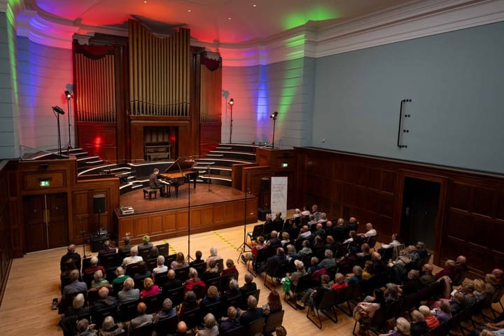 Audience watching a pianist perform on stage at Cowdray Hall under coloured lights.