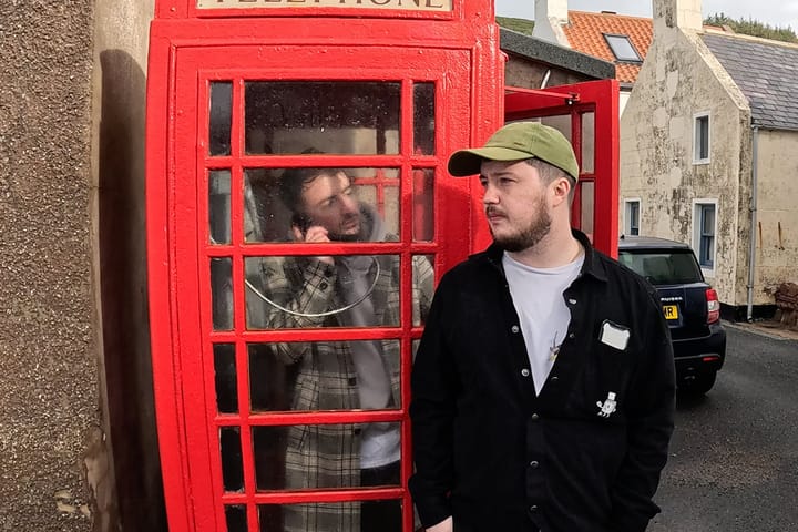 Jackill in red phone box with Vagrant Real Estate standing beside it in Pennan