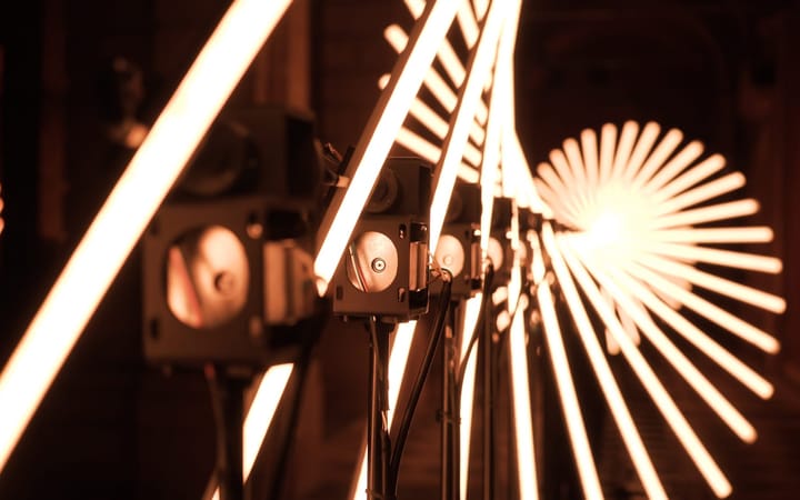 Stage lighting equipment projecting warm orange light beams creating starburst patterns and diagonal lines against dark background.