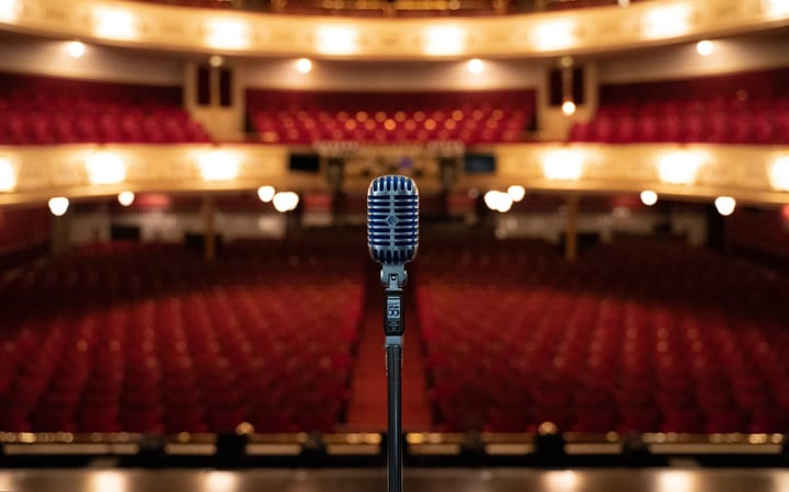 A vintage microphone on stage at His Majesty's Theatre, with the empty red-seated auditorium behind.