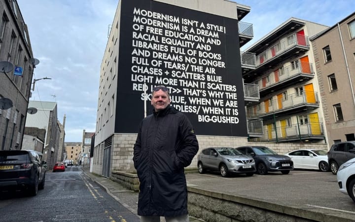 Martyn Reed stands in front of a text-based mural on an Aberdeen street.