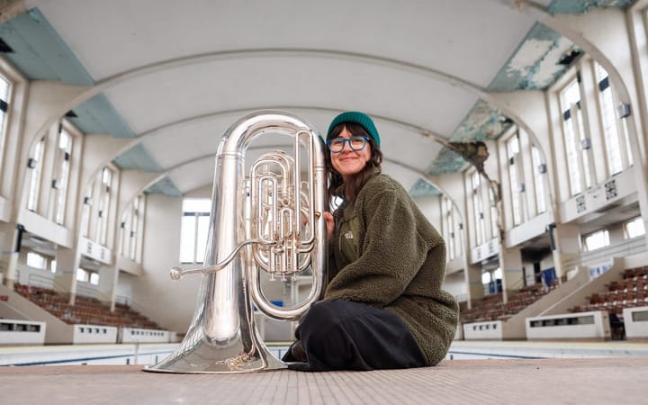 Danielle Price kneels with her tuba on the tiled floor of Bon Accord Baths' empty Art Deco pool hall.