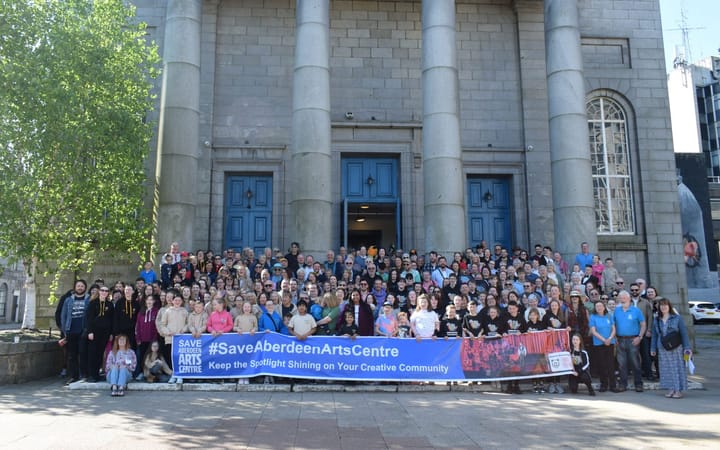 A large crowd on the steps of Aberdeen Arts Centre holding a Save Aberdeen Arts Centre banner.