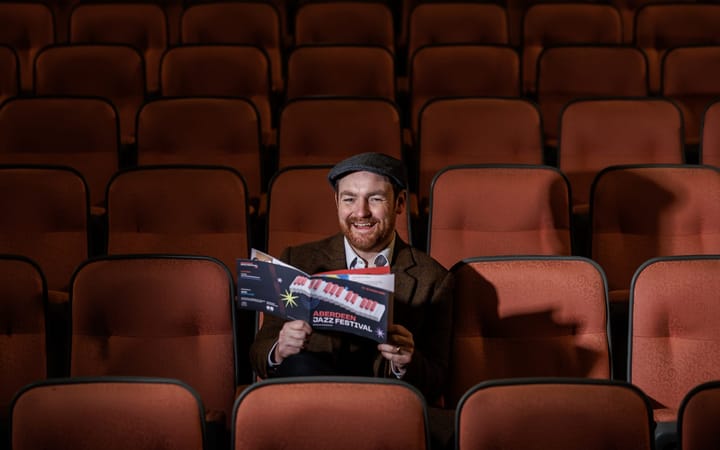 A man in a flat cap reads an Aberdeen Jazz Festival programme in an empty auditorium.