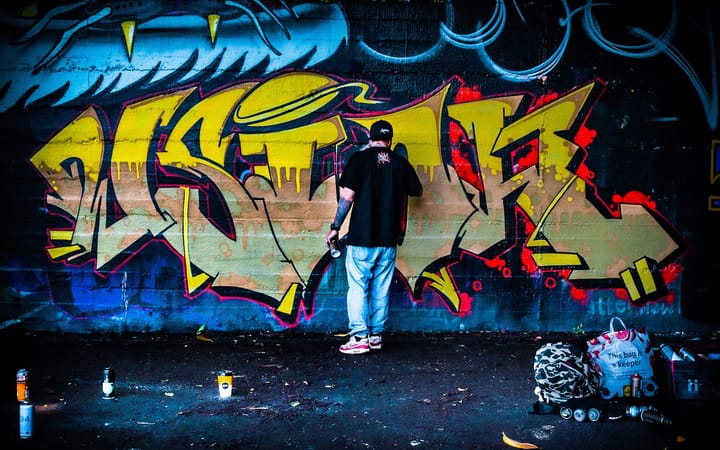A graffiti artist spray-painting a large yellow and red mural on a wall
