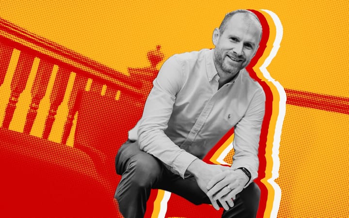Black-and-white photo of Mark Reynolds crouching against a red and yellow halftone room.